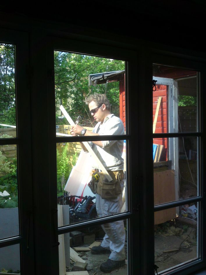 Det er Rasmus tømrer ,der står uden-for i gården .Nu er det store vindue sat i.Det fylder næsten hele væggen.